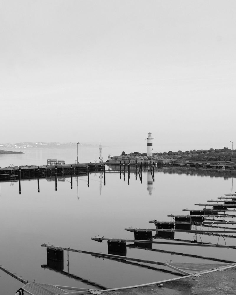 A still harbour in morning mist with a moored sailboat and a small lighthouse