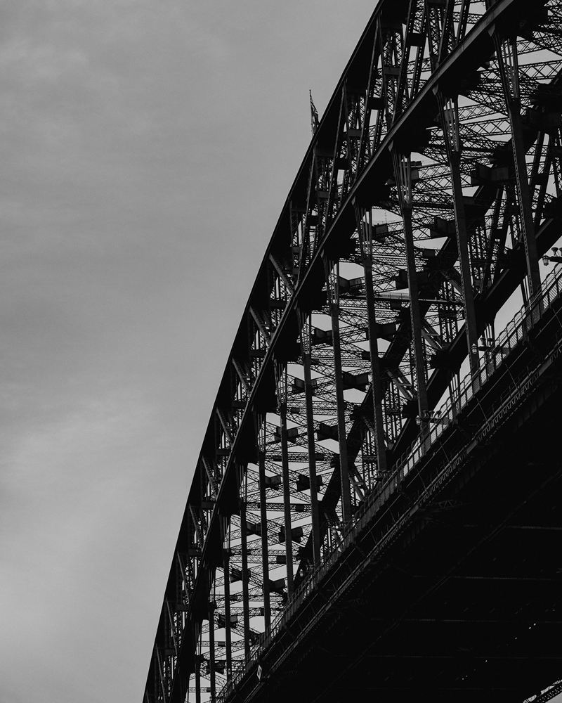 Steel arch of the Sydney Harbour Bridge seen from below against an overcast sky