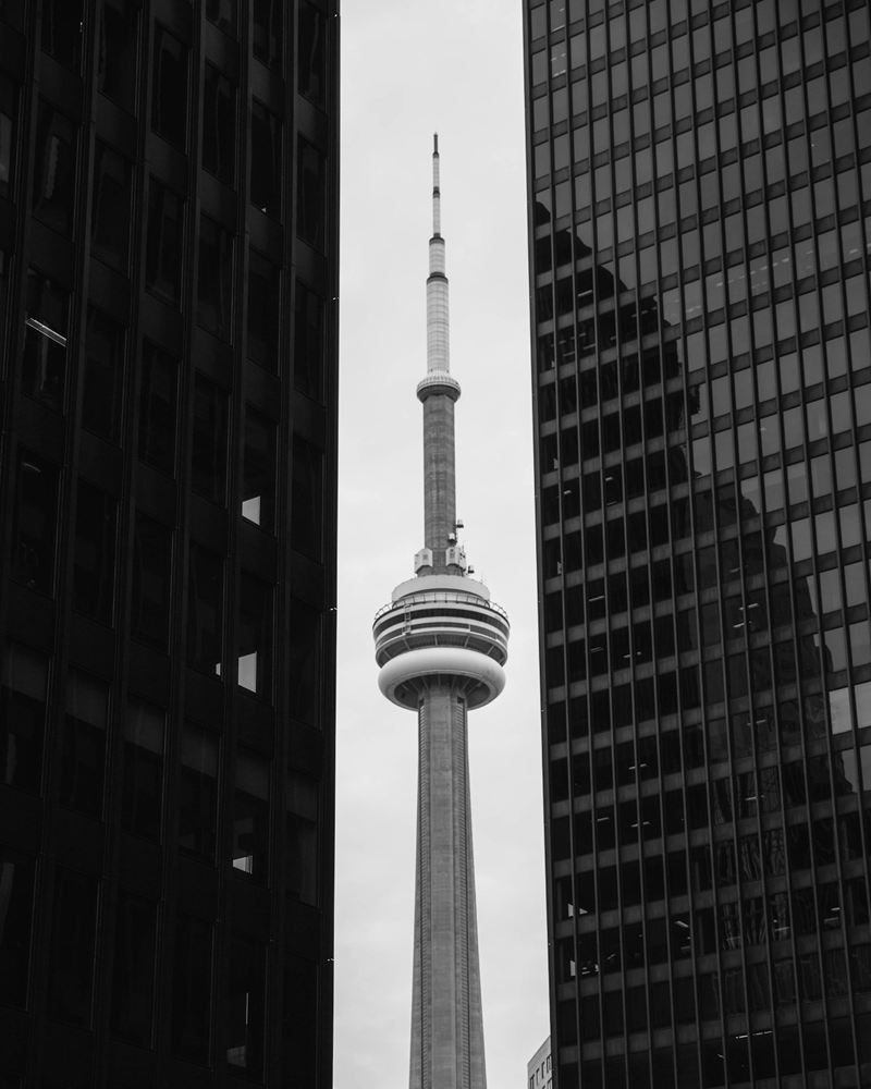 The CN Tower framed between two dark curtain-wall office towers in Toronto's financial district