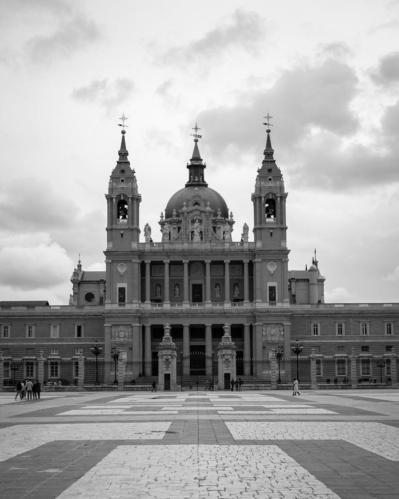 Almudena Cathedral in Madrid seen across the paved Plaza de la Armería under an overcast sky