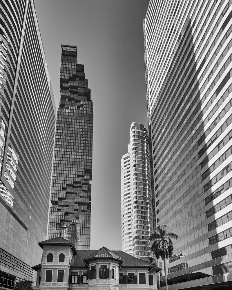 Bangkok's pixelated MahaNakhon tower rising between office towers above a colonial-era mansion in the Silom-Sathorn business district