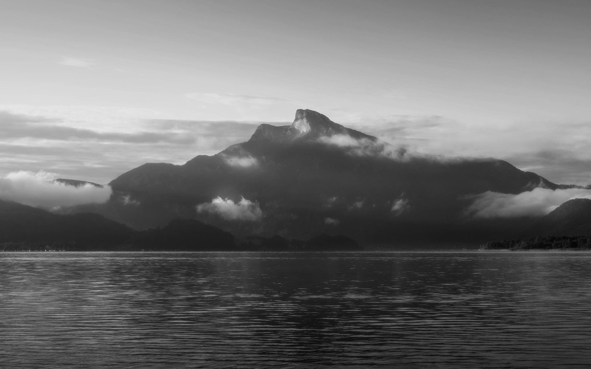 A mountain rising from still lake water at dawn, in black and white